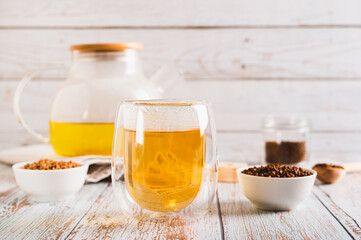 Fresh buckwheat tea in a glass and teapot and granules in a bowl on the table