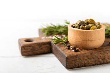 Capers in a bowl on a wooden kitchen table. Capers with sea salt and rosemary. Pickled capers.Mediterranean cuisine ingredient. Organic spices and seasonings. Copy space.