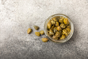 Capers in a glass jar on a wooden kitchen table. Capers with sea salt and rosemary. Pickled capers.Mediterranean cuisine ingredient. Organic spices and seasonings. Copy space.