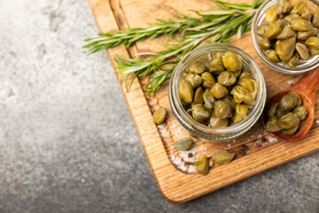 Capers in a glass jar on a wooden kitchen table. Capers with sea salt and rosemary. Pickled capers.Mediterranean cuisine ingredient. Organic spices and seasonings. Copy space.