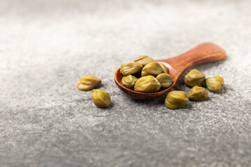 Capers in a wooden spoon on a wooden kitchen table. Capers with sea salt and rosemary. Pickled capers.Mediterranean cuisine ingredient. Organic spices and seasonings. Copy space.