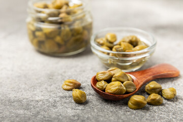 Capers in a bowl on a wooden kitchen table. Capers with sea salt and rosemary. Pickled capers.Mediterranean cuisine ingredient. Organic spices and seasonings. Copy space.