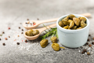 Capers in a bowl on a wooden kitchen table. Capers with sea salt and rosemary. Pickled capers.Mediterranean cuisine ingredient. Organic spices and seasonings. Copy space.