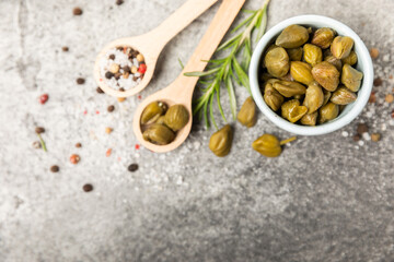 Capers in a bowl on a wooden kitchen table. Capers with sea salt and rosemary. Pickled capers.Mediterranean cuisine ingredient. Organic spices and seasonings. Copy space.