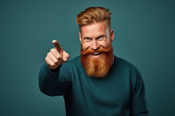 A man with a striking red beard and styled hair winks and points towards the camera, displaying a playful and engaging demeanor against a teal background