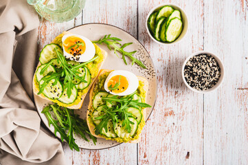 Sandwiches on ciabatta with avocado, cucumber, egg and arugula on a plate top view