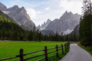 Scenic hiking trail along alpine meadow secured by wooden fence in panoramic valley Fischleintal near Moos. Panoramic view of majestic mountain ridges of Sexten Dolomites in Italian Alps. Wanderlust