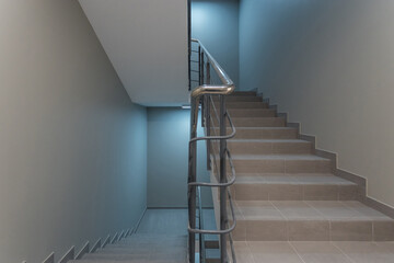 A corridor with light walls, beige floor tiles and a staircase with metal railings.