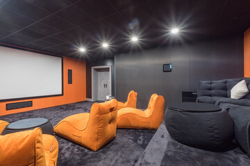 Modern home theater design with gray wall and floor decor. A huge screen, a gray sofa and orange...