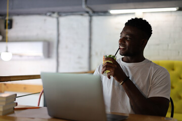 A cheerful young businessman using a laptop in a modern office, embodying professionalism and technology.