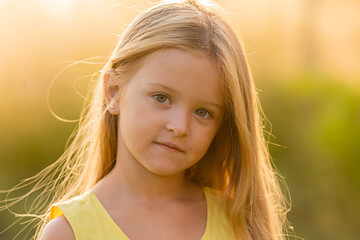 beautiful little girl with long blonde hair walks at sunset in the city park in summer