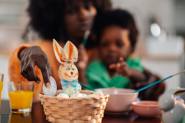 Close up of interracial mother putting easter egg into a basket on table.