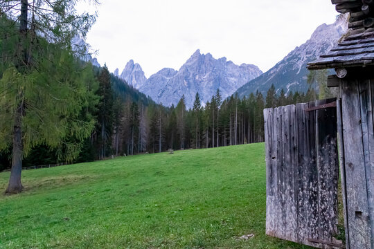 Wooden hut on alpine meadow with scenic view of majestic rugged mountain peaks of Sexten Dolomites, South Tyrol, Italy, Europe. Hiking in panoramic Fischleintal, Italian Alps. Idyllic conifer forest
