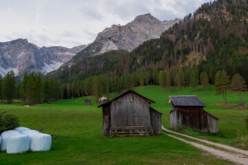 Scenic hiking trail along wooden huts on idyllic alpine meadow with awe view of majestic mountain...
