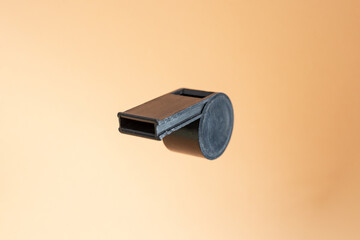 Black plastic whistle isolated on beige background, soft focus close up
