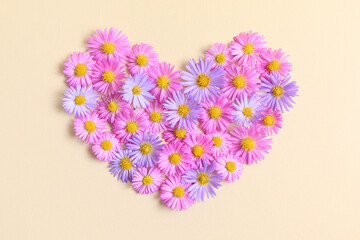 Heart made of pink and purple asters flowers on beige background. Creative spring idea, stylish trendy greeting card. Natural minimal concept. Flowers heart. Flat lay, top view.