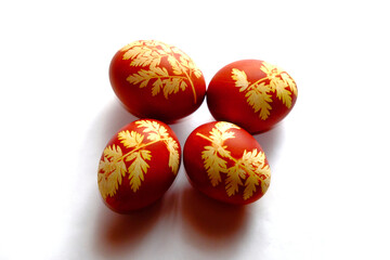 Obraz na płótnie Canvas The image shows four red eggs with intricate yellow leaf patterns displayed against a white background.