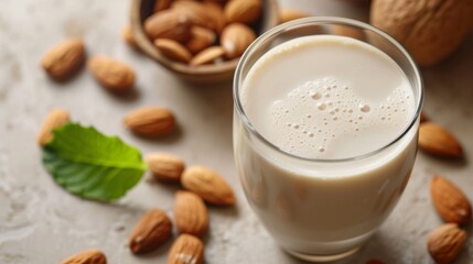 Almond milk in a glass with scattered almonds and a bowl in the backdrop, alternative plant-based vegan lactose-free milk