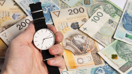 Watch with a white shield kept in hand against the background of scattered Polish banknotes (selective focus)