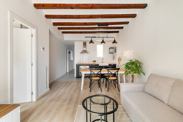 Horizontal shot compact apartment with combined dining room kitchen with sofa and coffee table and modern kitchen with loft-style beams and light walls. Concept of modern design in new apartments