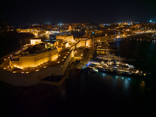 Aerial view of illuminated Fort St Angelo at night in Valletta. Side view on the fort and fortified Birgu town. Grand harbor with luxury super yachts moored. Date: 22.10.2023 Valletta, Malta.