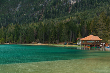 Turquoise water alpine lake Toblacher See with restaurant in Dolomiti mountains, Belluno, Veneto, Italy on spring day. Lake Lago di Dobbiaco in the forest in Dolomites in Italian Alps