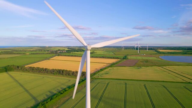 AERIAL, CLOSE UP: Rotating wind turbine on a wind farm in the English countryside. Spinning white blades of a windmill above picturesque farmland. Harnessing the wind to generate electric energy.