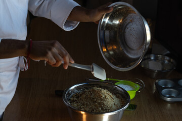 Photograph of the hands of a male chef, who is preparing a baked cake, mixing cookies with nuts in a bowl in his kitchen