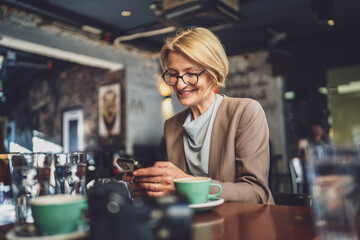 Mature Blonde causacian Woman use Smartphone at Cafe while sit alone