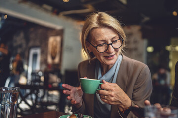 one mature caucasian blonde woman have a cup of coffee sit at cafe