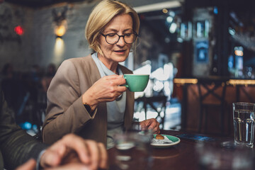 one mature caucasian blonde woman have a cup of coffee sit at cafe