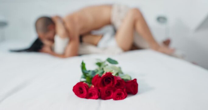 Couple, red roses and lying on bed for love, anniversary or valentines day in romance, embrace or trust at home. Romantic man and woman in bedroom intimacy, passion or bonding with flowers at house
