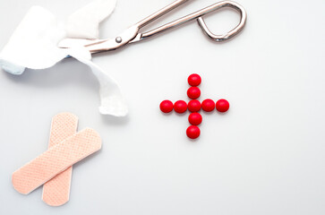 medicine concept, instruments used in medicine, scissors cutting a band aid, patch and red sign for health made from pills isolated on white background