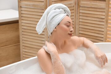 Beautiful woman taking bath with foam in tub indoors, space for text