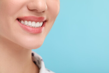 Woman with clean teeth smiling on light blue background, closeup. Space for text