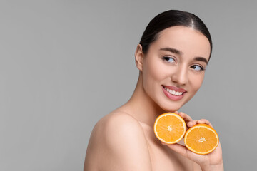 Beautiful young woman with pieces of orange on grey background. Space for text