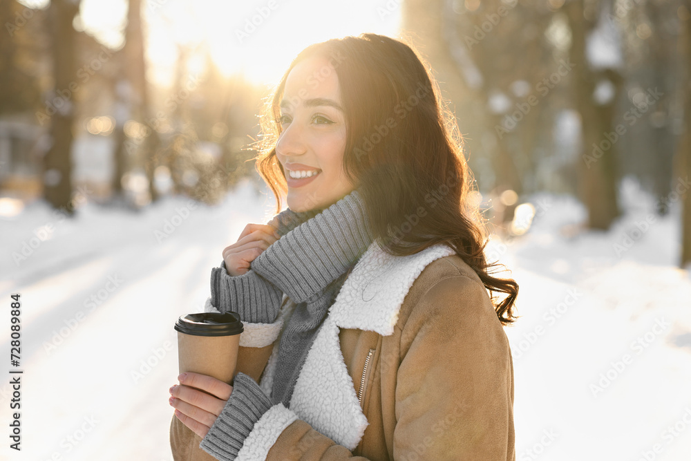 Wall mural Portrait of smiling woman with paper cup of coffee in snowy park