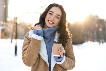 Portrait of smiling woman with paper cup of coffee in snowy park