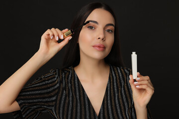 Obraz premium Beautiful young woman applying mascara on black background