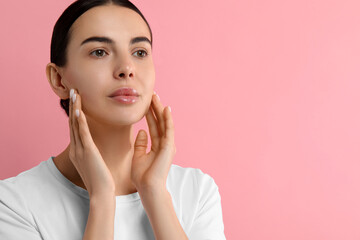 Woman with dry skin checking her face on pink background, space for text