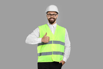 Engineer in hard hat showing thumb up on grey background