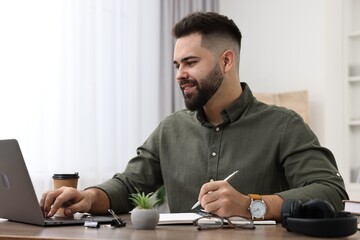 Fototapeta premium E-learning. Young man taking notes during online lesson at wooden table indoors