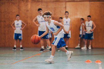 A junior basketball player dribbling a ball and practicing on court. - obrazy, fototapety, plakaty