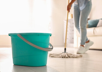 Plastic bucket and woman mopping floor in living room, closeup. Cleaning supplies © New Africa