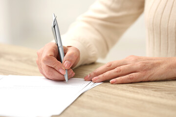 Senior woman signing Last Will and Testament at wooden table indoors, closeup