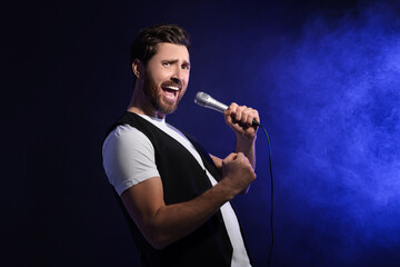 Handsome man with microphone singing on dark blue background