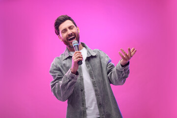 Handsome man with microphone singing on pink background