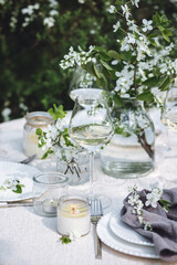 Romantic elegant luxury wedding table decor with white fresh spring blooming cherry apple tree flowers. Glass, candles, floral decoration for special marriage holiday event. No plastic zero waste