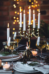 Fototapeta na wymiar Beautiful table setting for family Christmas dinner at home. Cozy atmosphere, candlelight. Wine glasses, vintage chandelier, elegant interior. Fir tree branches, wooden furniture, dark, bokeh