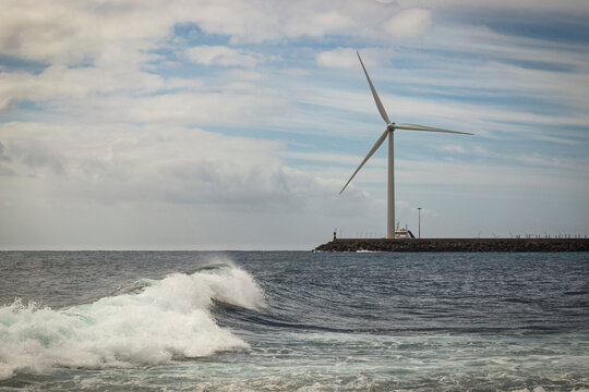 SPAIN / Canary Islands / Gran Canaria. Large wind turbine anchored on land near the seashore, in the town of Arinaga. Foreground of waves coming in